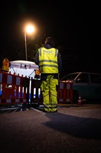 Person in safety clothing monitors a construction site at night under artificial light,