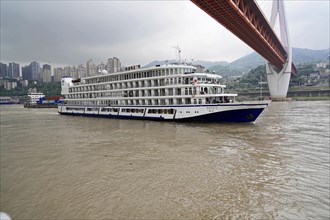 Chongqing, Chongqing Province, China, Cruise ship on a river under a large bridge on an overcast