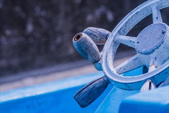 Old white steering wheel on blue boat in front of blurred concrete wall in South Korea