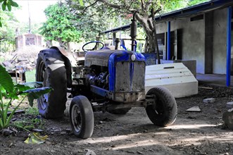 Ometepe Island, Nicaragua, An old, blue tractor stands in front of rural buildings, Central