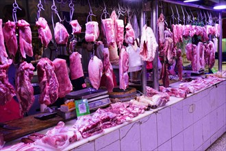 Chongqing, Chongqing Province, China, Pieces of meat hanging on hooks in an internally lit market