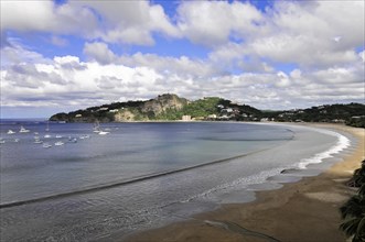 San Juan del Sur, Nicaragua, Clear waves rolling towards a beach with a bay full of yachts in the