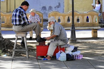 Leon, Nicaragua, A shoeshine boy serves a customer on the street under the shade of the trees,