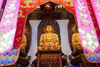 Jade Buddha Temple, Shanghai, Buddha in meditation posture behind colourful curtains on a richly