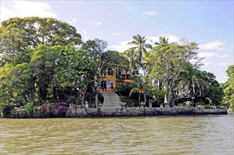 Granada, Nicaragua, Colourful house on the lakeshore with a boat in front, surrounded by palm