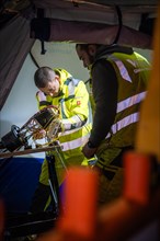 Worker carrying out electrical installation work in an illuminated work tent during the night,