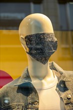 Mannequin with a corona mask on its face in a shop window of a fashion shop in the city centre of