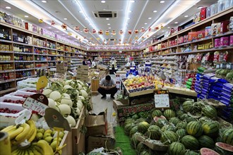 Shanghai, China, Asia, A person sits in the middle of a richly stocked fruit and vegetable shop,