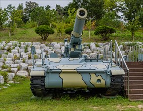 Closeup of military tank with camouflage paint next to wooden stairway in public park in Nonsan,