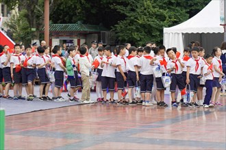 A group of schoolchildren in uniforms with red scarves stand in order on a sports field, Chongqing,