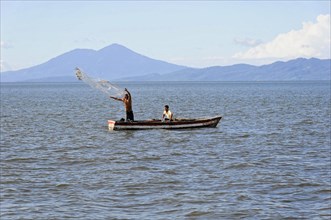 Lake Nicaragua, Two men in a boat casting a fishing net on a lake, mountains in the background,