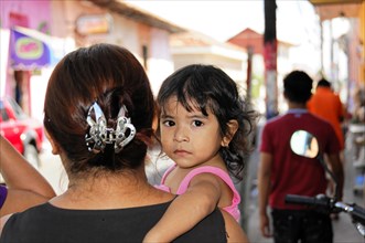 Leon, Nicaragua, A child looks over the shoulder of a woman in a busy city street, Central America,