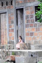 Leon, Nicaragua, A small child sits alone at the entrance of a house with brick walls, Central