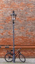 Candelabra with attached bicycle in front of a brick wall, Berlin, Germany, Europe