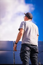 A man inspects a solar panel under a blue sky, solar systems construction, trade, Muehlacker,
