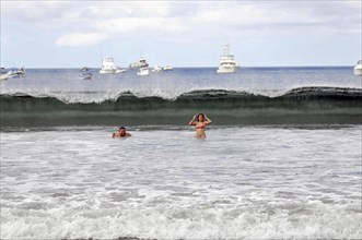 San Juan del Sur, Nicaragua, Swimmers in the sea with a big wave in the background and boats on the