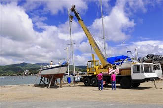 San Juan del Sur, Nicaragua, A crane lifts a boat in the harbour, Workers watch the operation,