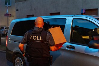 A customs officer carries a cardboard box to an official vehicle in the evening, The Cologne police