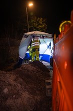 Worker in reflective clothing working at night in an excavation pit under artificial lighting,
