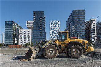 Excavator in front of The Barcode Project Oslo, modern residential and commercial building,