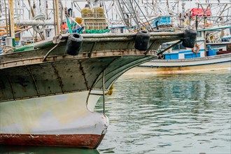 Closeup of bow of large fishing vessel anchored in harbor with other boats and rigging in the