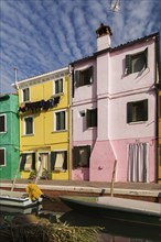 Moored boats on canal lined with pink, yellow and green stucco houses decorated with striped