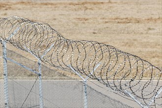 View of a barbed wire fence against a dry background, symbolising security and demarcation