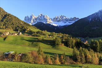 Sunlit village in a valley below a snow-covered mountain range, Italy, Trentino-Alto Adige, Alto