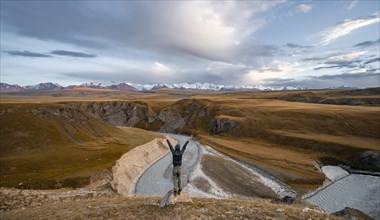 Tourist stretching his arms in the air, mountain valley with Sary Jaz river, high glaciated