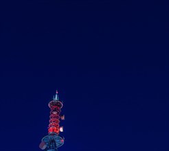 Low angle night view of large communication array tower lit up in red lights with dark blue sky in