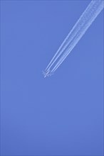 Passenger aeroplane, four-striped with condensation streaks in the blue sky, North