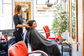Side view photo of a hairdresser attending a woman sitting on chair in the salon