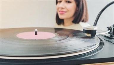 Close-up of a turntable with a vinyl record playing, woman in the background, AI generated