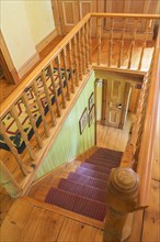 Looking down staircase with maple wood railings and pine wood steps covered with multi-coloured