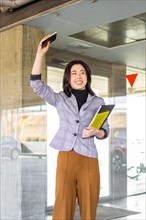 Woman in formal suit saying goodbye to a person outdoors. Portrait of smiling business girl waving