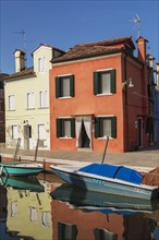 Moored boats on canal lined with red and yellow stucco houses, Burano Island, Venetian Lagoon,
