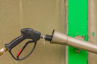 Black handle of car wash high pressure water gun with long nozzle inserted into metal cylinder in