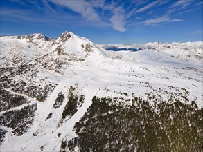 Wide-angle aerial view of snow-covered mountains and forest areas under a blue sky, Grau Roig,