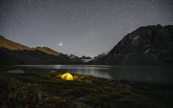 Yellow illuminated camping tent under a starry sky at the mountain lake Ala Kul Lake, mountain