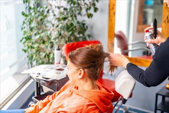 Unrecognizable female hairdresser applying hairspray to a client's hair in the salon