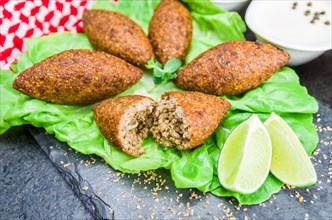 Delicious Lebanese (Arabic) food, kibbeh (kibe) with sauces and lemon on black slate stone and