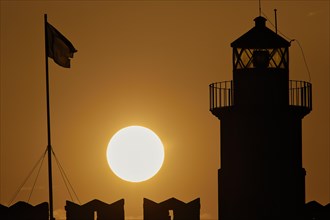The silhouette of a lighthouse with a flag against the background of a round sunrise, sunrise,