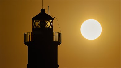 A lighthouse stands as a dark silhouette next to the round sun at sunrise, sunrise, dawn, Fort of