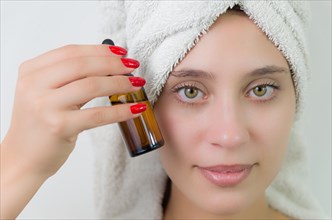 Happy young woman with towel on head holding amber glass bottle of skin serum. Beautiful young