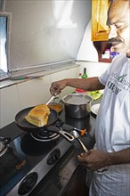 Indian man frying a dosa or pancake in a ship's galley, traditional Kerala dish, Kerala, India,
