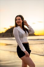 Vertical photo of a distracted chic sensual woman posing on the beach during sunset