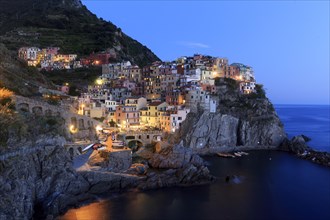 A Mediterranean village on the coast is romantically illuminated by the sea at nightfall, Italy,