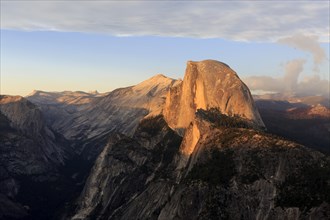 The setting sun bathes Half Dome in orange hues, surrounded by dramatic clouds, Yosemite National