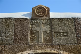 A stone cross with engraved symbols and dates against a clear blue sky, Panagia Church, St Mary's