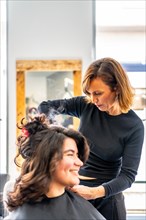Vertical photo of a hairstylist curling the hair of a woman sitting in the salon